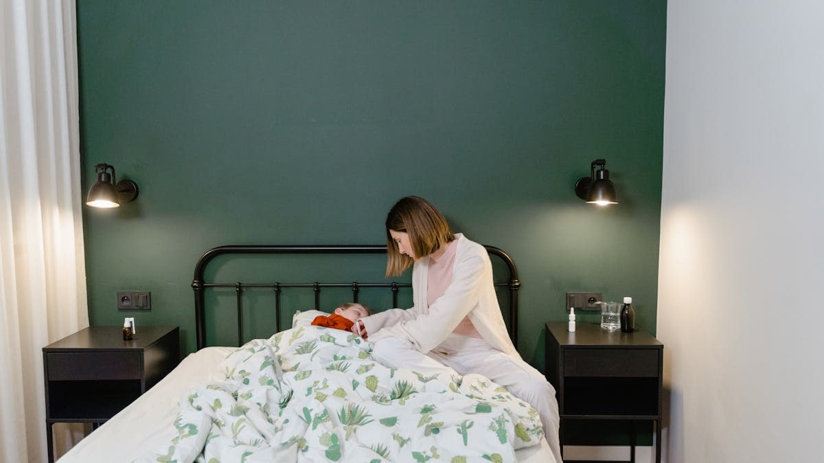A mother cares for her child with a fever in a warm, cozy bedroom setting.